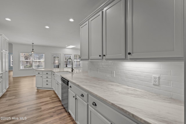 kitchen with backsplash, a peninsula, a sink, light wood-style floors, and stainless steel dishwasher