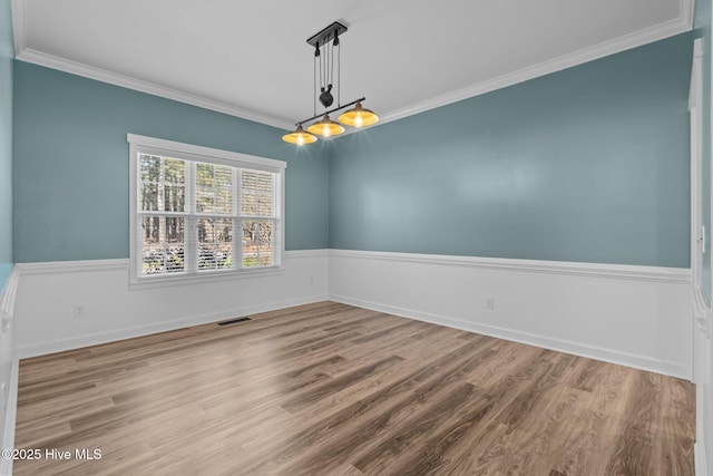 empty room featuring ornamental molding, visible vents, baseboards, and wood finished floors