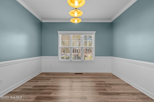 spare room with wood finished floors, visible vents, and crown molding