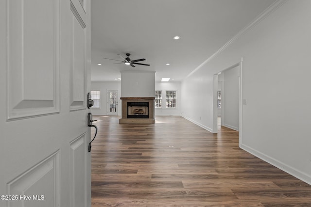 living area with crown molding, recessed lighting, a fireplace with raised hearth, dark wood-type flooring, and baseboards