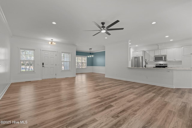 unfurnished living room with recessed lighting, ceiling fan with notable chandelier, baseboards, ornamental molding, and light wood finished floors