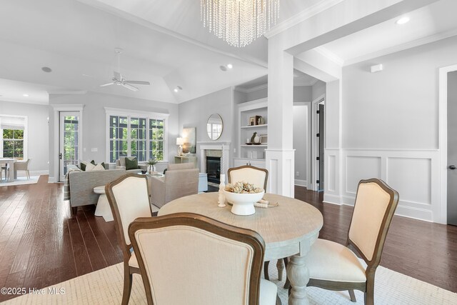 2900 Legends Dr, Southport, NC 28461 - dining room featuring a fireplace, dark wood-style flooring, recessed lighting, ceiling fan, and wainscoting