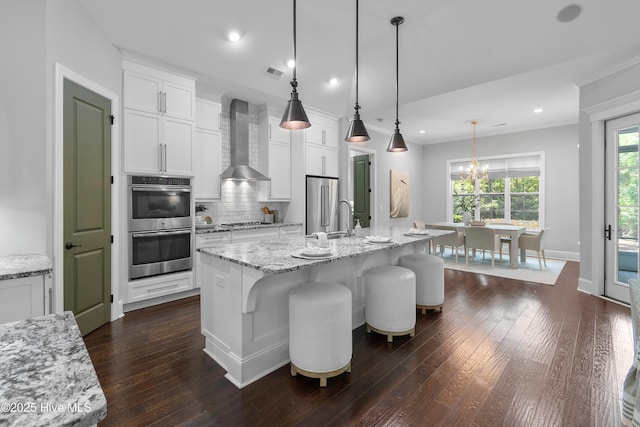 2900 Legends Dr, Southport, NC 28461 - kitchen with wall chimney exhaust hood, stainless steel appliances, decorative backsplash, a chandelier, and white cabinetry