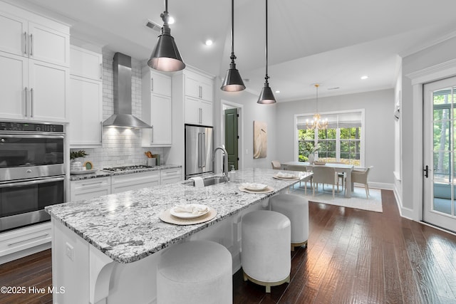2900 Legends Dr, Southport, NC 28461 - kitchen featuring wall chimney exhaust hood, appliances with stainless steel finishes, a sink, a chandelier, and an island with sink