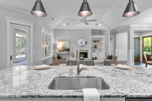 2900 Legends Dr, Southport, NC 28461 - kitchen featuring a sink, a fireplace, light stone countertops, crown molding, and hanging light fixtures