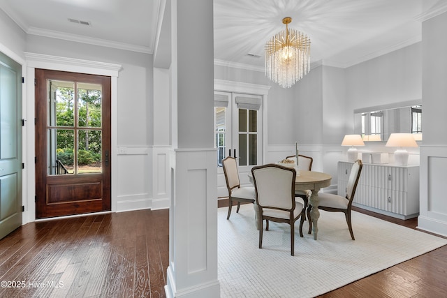 2900 Legends Dr, Southport, NC 28461 - dining room featuring dark wood-type flooring, a chandelier, a wainscoted wall, a decorative wall, and ornamental molding