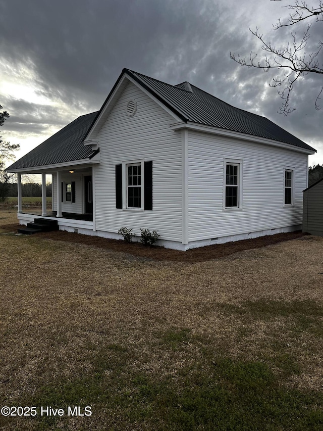 view of side of property with a porch, crawl space, metal roof, and a lawn