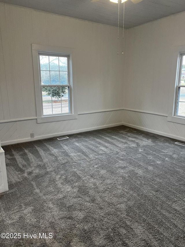 unfurnished room with a healthy amount of sunlight, dark carpet, and visible vents
