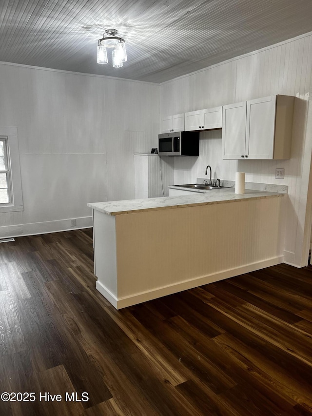 kitchen featuring baseboards, stainless steel microwave, dark wood-type flooring, a peninsula, and a sink