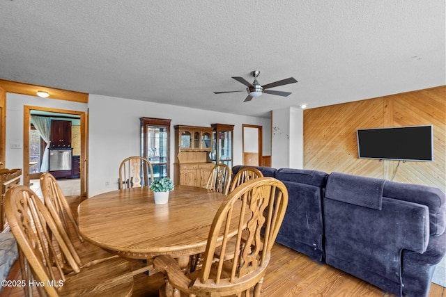 dining area with wooden walls, a ceiling fan, light wood-type flooring, and a textured ceiling