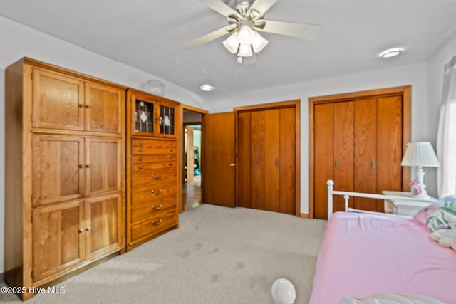 bedroom featuring light carpet, two closets, and ceiling fan