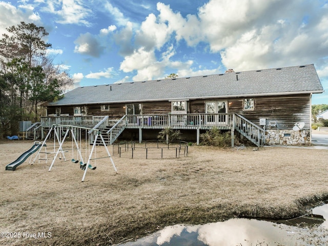 back of property featuring a deck, stairway, playground community, and a shingled roof