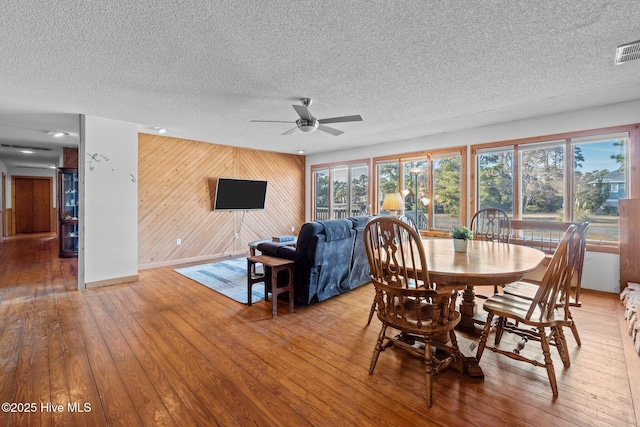 dining room with baseboards, ceiling fan, wood walls, a textured ceiling, and wood-type flooring