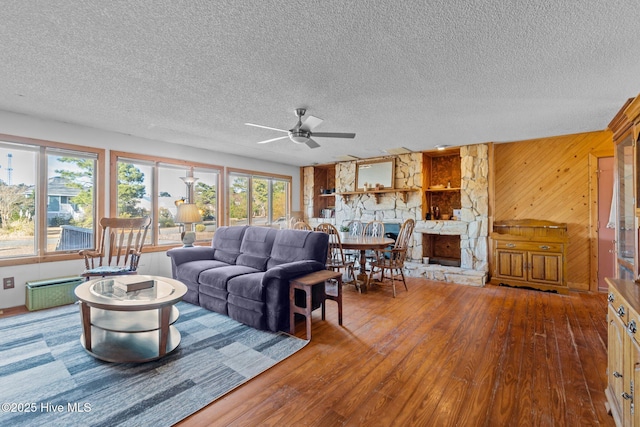 living area featuring wooden walls, a fireplace, wood finished floors, a textured ceiling, and a ceiling fan