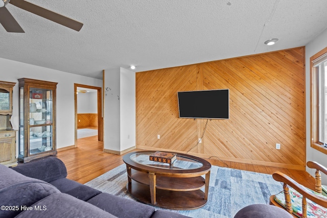 living room featuring a textured ceiling, wood finished floors, a ceiling fan, and wood walls