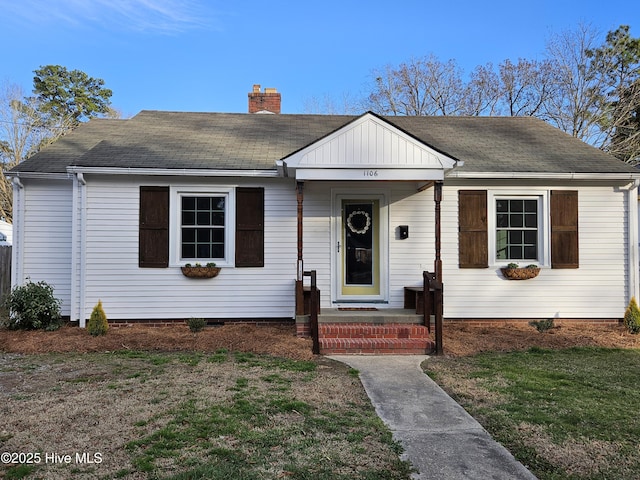 bungalow-style home featuring a shingled roof, a chimney, and a front lawn