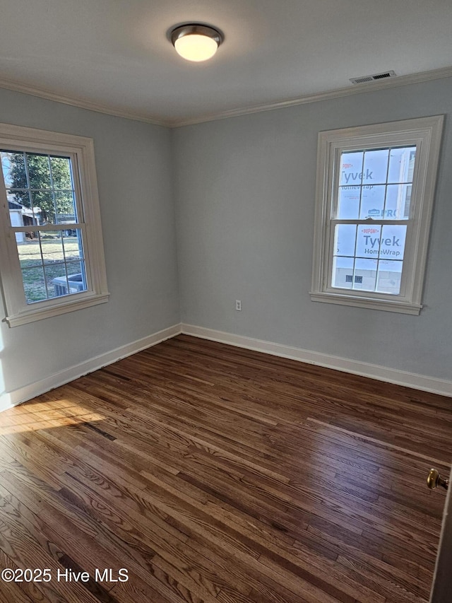 empty room featuring ornamental molding, visible vents, dark wood finished floors, and baseboards