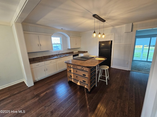 kitchen with dark wood finished floors, crown molding, dark countertops, white cabinets, and a sink