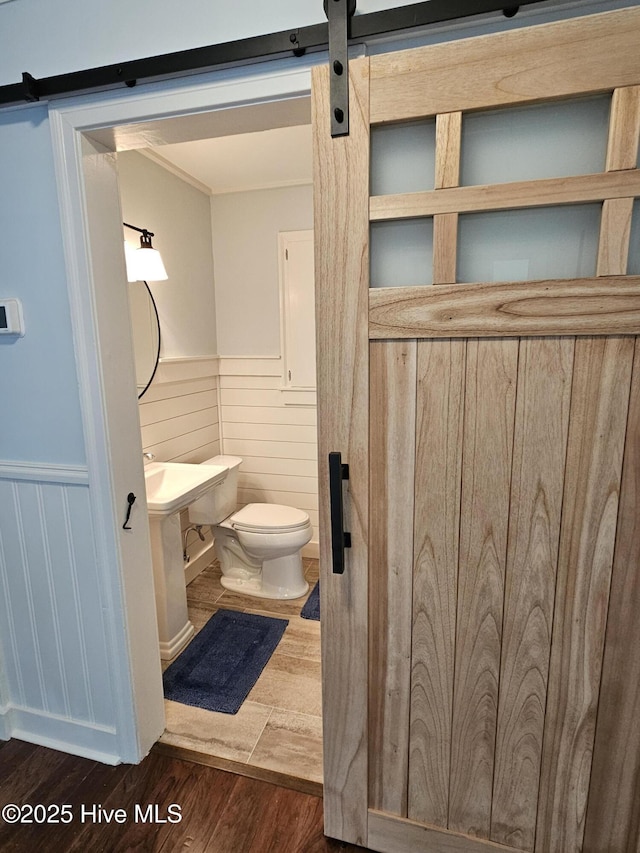 half bathroom with wainscoting, toilet, and wood finished floors