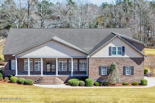 view of front of house with french doors, brick siding, covered porch, and a front yard