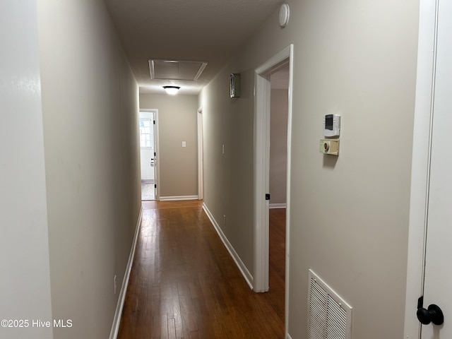 hallway featuring attic access, visible vents, dark wood finished floors, and baseboards