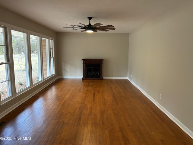 unfurnished living room with dark wood-type flooring, a fireplace with raised hearth, plenty of natural light, and baseboards