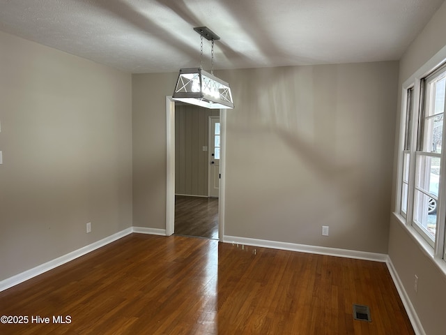 unfurnished dining area featuring dark wood-style flooring, visible vents, and baseboards