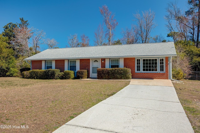 ranch-style home featuring brick siding, driveway, a front lawn, and roof with shingles