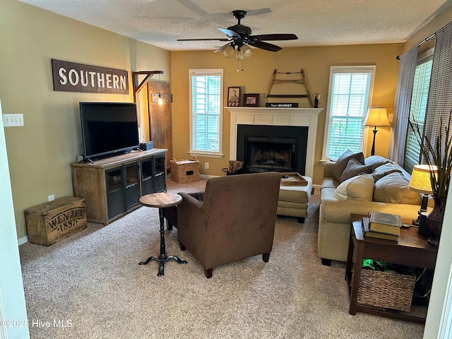 living area with a textured ceiling, ceiling fan, a fireplace, and carpet flooring