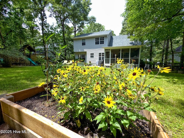 back of house featuring a sunroom, roof with shingles, a playground, and a yard