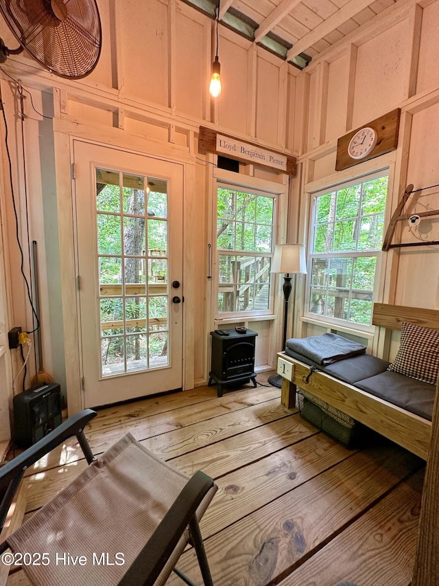 entryway with a high ceiling, wood walls, a wood stove, and light wood-style floors