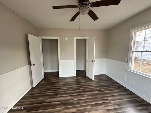 unfurnished bedroom with a wainscoted wall, ceiling fan, dark wood-style flooring, and a closet