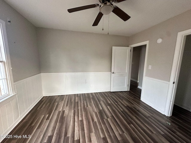 empty room with dark wood-type flooring and a wainscoted wall