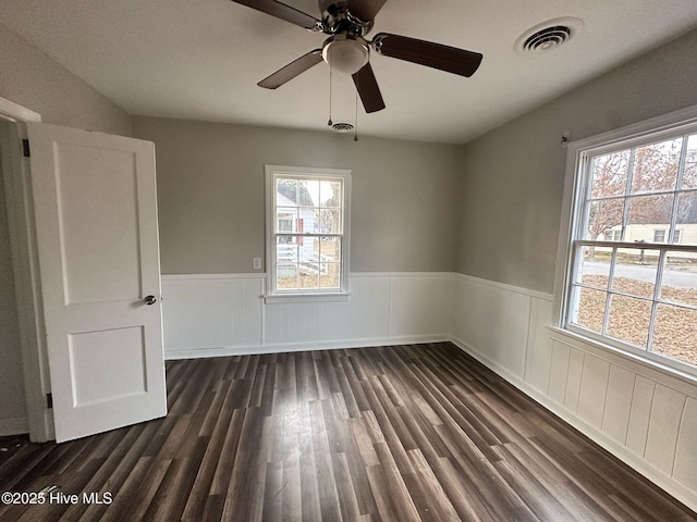 spare room with dark wood-style floors, a wainscoted wall, and visible vents