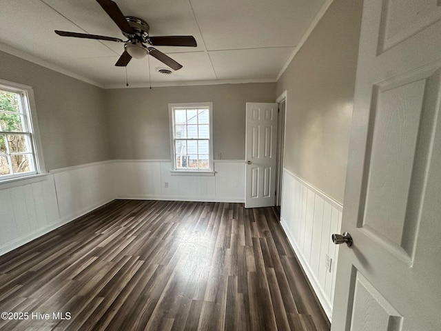 empty room with a wainscoted wall, dark wood-style flooring, and a wealth of natural light