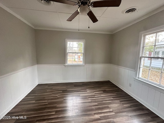 empty room featuring dark wood-style floors, wainscoting, crown molding, and visible vents