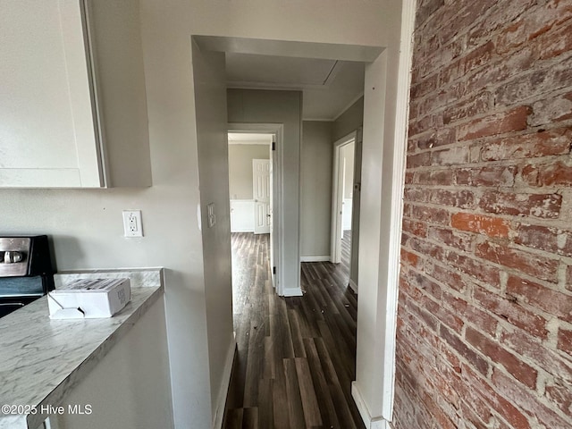 hall featuring brick wall, dark wood-style flooring, and baseboards