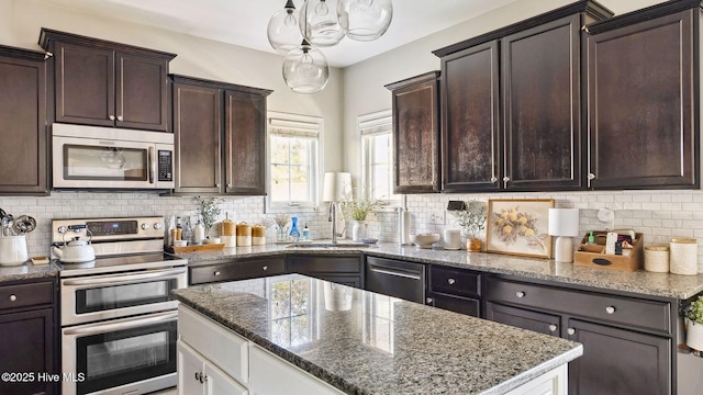 kitchen with dark brown cabinetry, decorative backsplash, appliances with stainless steel finishes, light stone countertops, and a sink