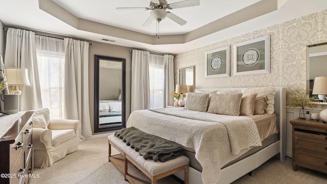 bedroom featuring a tray ceiling, visible vents, a ceiling fan, light carpet, and wallpapered walls