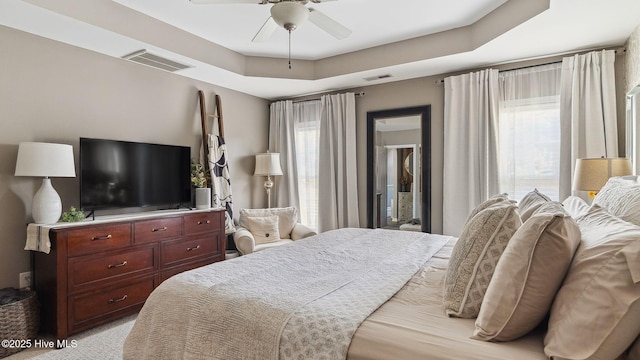 bedroom with a raised ceiling, visible vents, and multiple windows