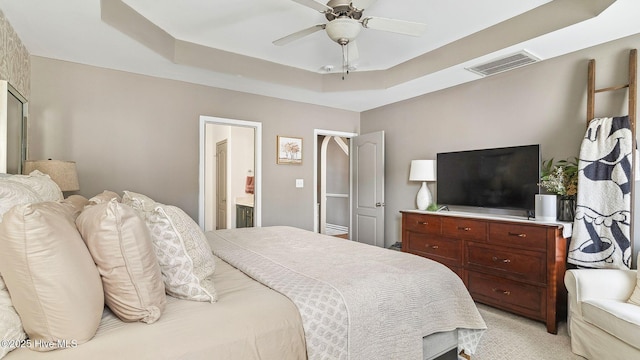 bedroom with ensuite bathroom, ceiling fan, light colored carpet, visible vents, and a raised ceiling