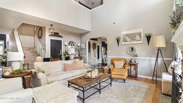 living area featuring visible vents, arched walkways, stairway, wood finished floors, and a high ceiling