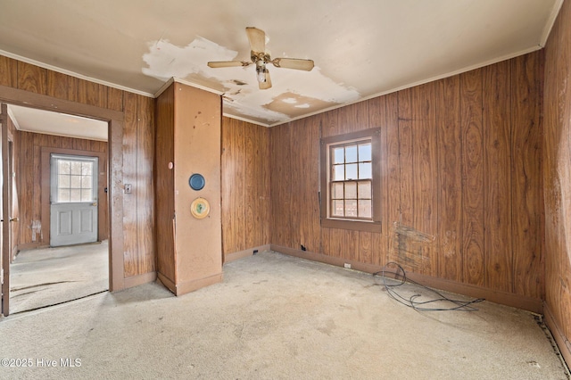 spare room with carpet floors, wood walls, a ceiling fan, baseboards, and ornamental molding