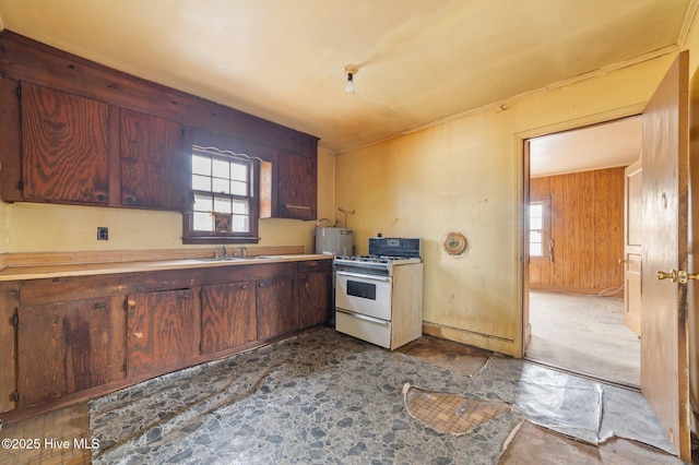 kitchen with gas range gas stove, light countertops, stone finish floor, a sink, and wooden walls