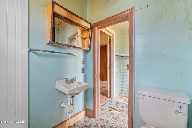 half bath featuring toilet, stone finish floor, and a sink