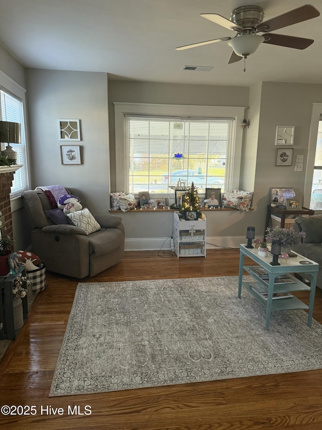 living room featuring baseboards, wood finished floors, visible vents, and a ceiling fan