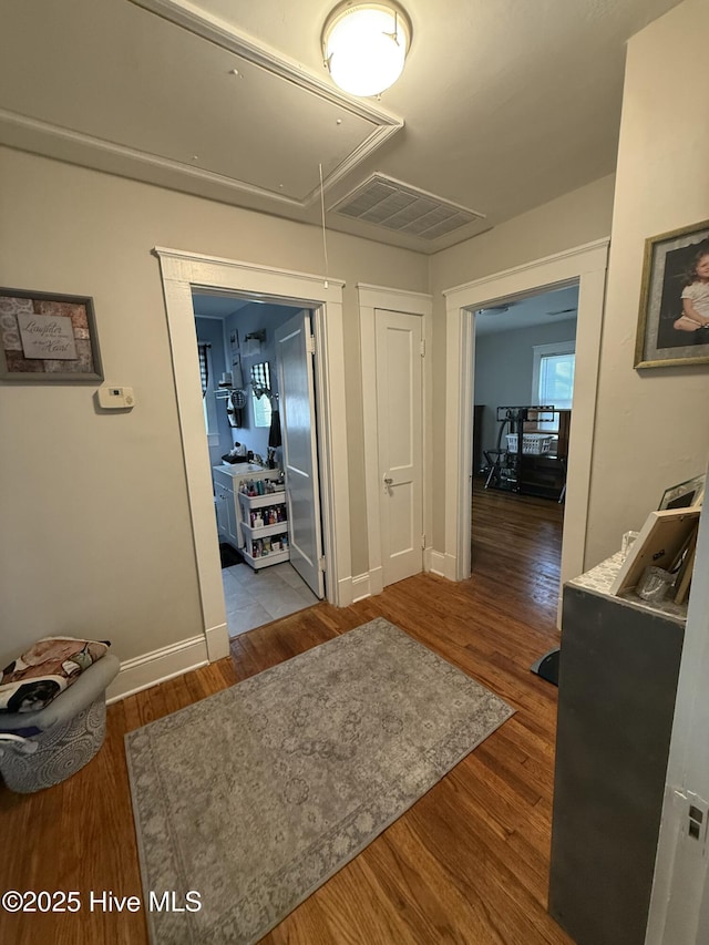 hall with attic access, visible vents, baseboards, and wood finished floors