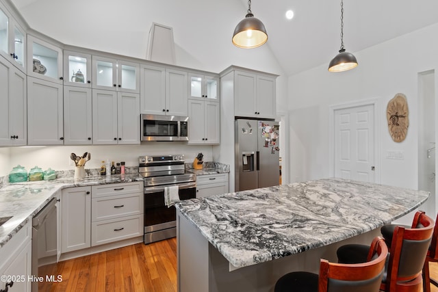 kitchen featuring vaulted ceiling, hanging light fixtures, appliances with stainless steel finishes, light wood finished floors, and a kitchen bar