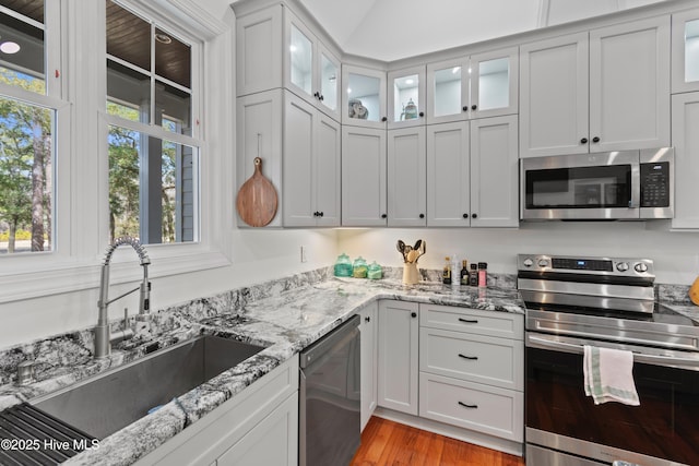 kitchen with light wood-style flooring, light stone counters, stainless steel appliances, white cabinetry, and a sink