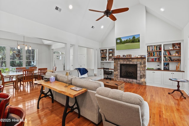 living room with high vaulted ceiling, visible vents, a stone fireplace, and light wood finished floors